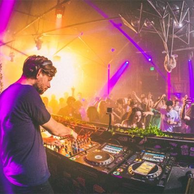 DJ legt Musik in einem Club auf, tanzende Menschen im Hintergrund