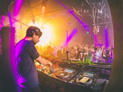 DJ legt Musik in einem Club auf, tanzende Menschen im Hintergrund