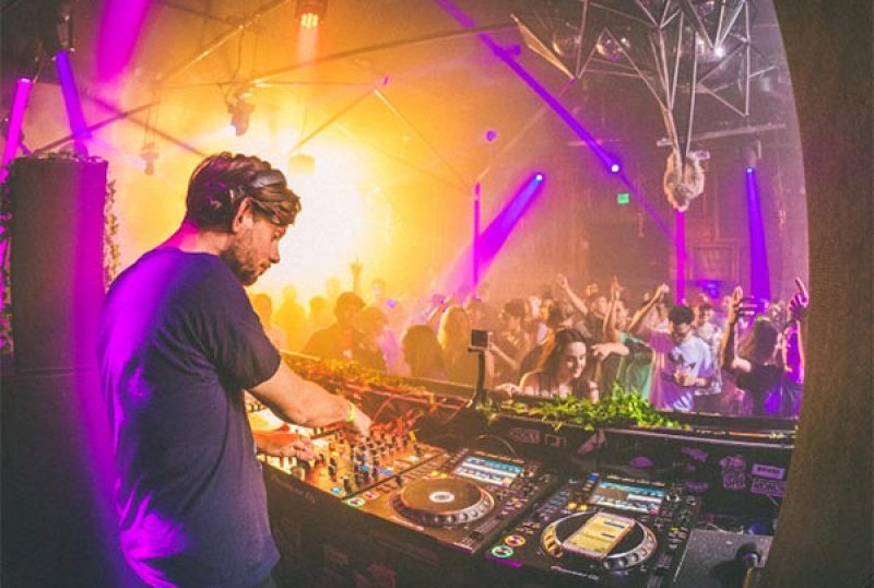 DJ legt Musik in einem Club auf, tanzende Menschen im Hintergrund